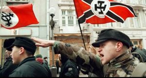 A man performing a Nazi salute at a rally with Nazi flags.